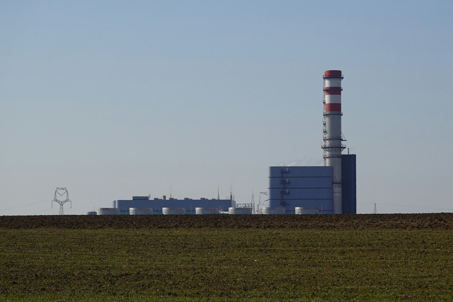 Planta de energía industrial con chimenea rayada detrás de un campo.